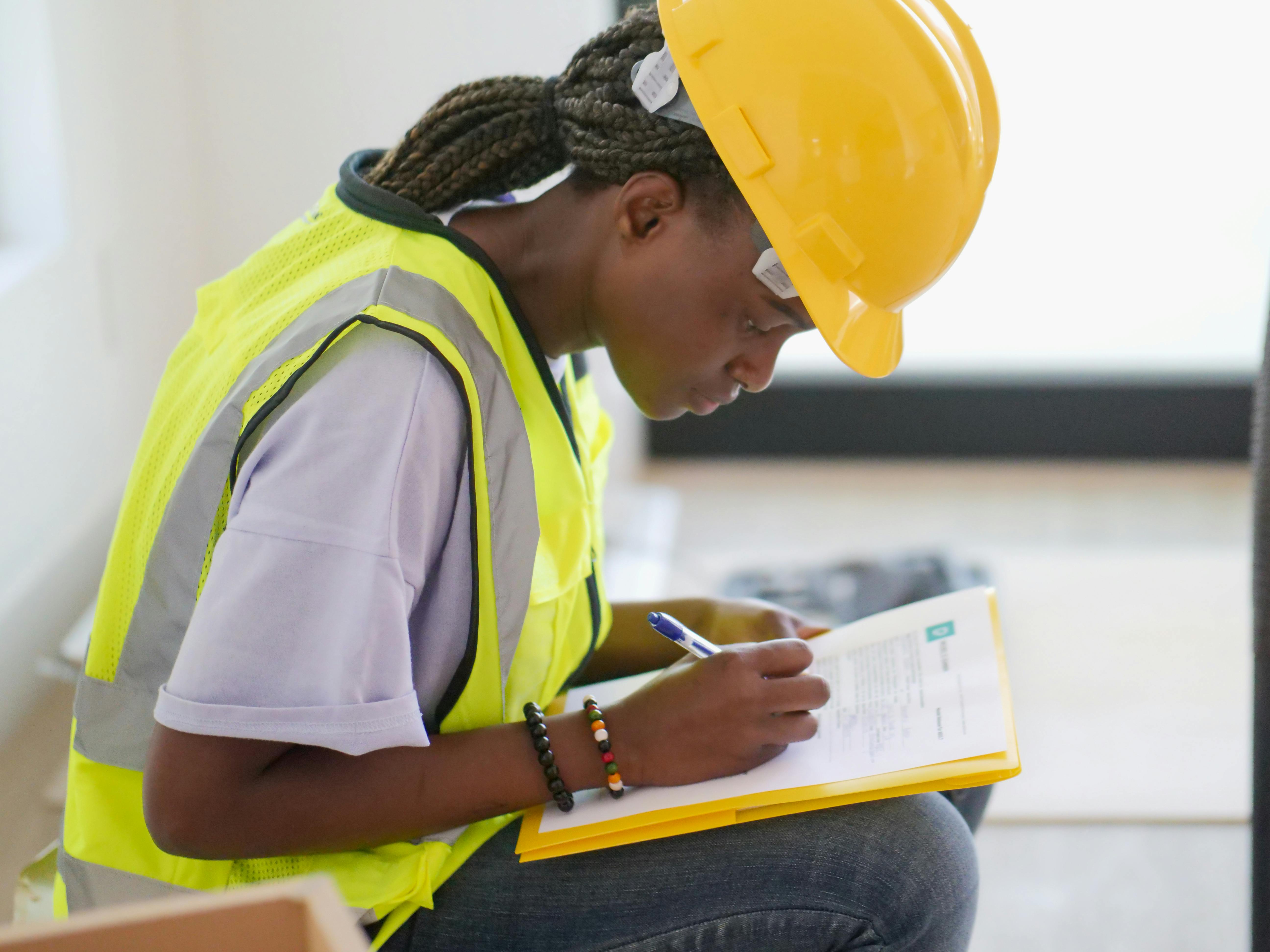 Student in safety vest and hard hat writing on a clipboard